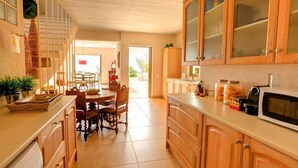 A kitchen with wooden cabinets, a dining table with chairs, and a microwave. - Villa 'Corali Ideales Resort' with Sea View, Wi-Fi and Air Conditioning (kefalonia)