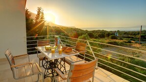 En balkon med et bord dækket til morgenmad, med udsigt over et smukt landskab med træer og et fjernt hav.
