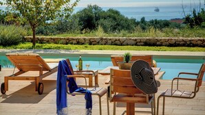 Zona junto a la piscina con sillas de descanso, una mesa y vista al mar.