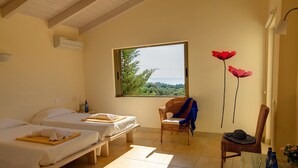 Una habitación con dos camas, una ventana con vistas, una silla y una mesa con botellas.
