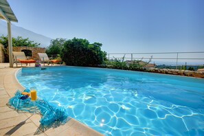 Una piscina con agua cristalina, un vaso de zumo de naranja y un muro de piedra.