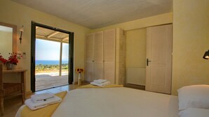 Ein Schlafzimmer mit Bett, einem Sessel, einem Tisch mit einer Vase, einer Tür und Blick ins Freie.