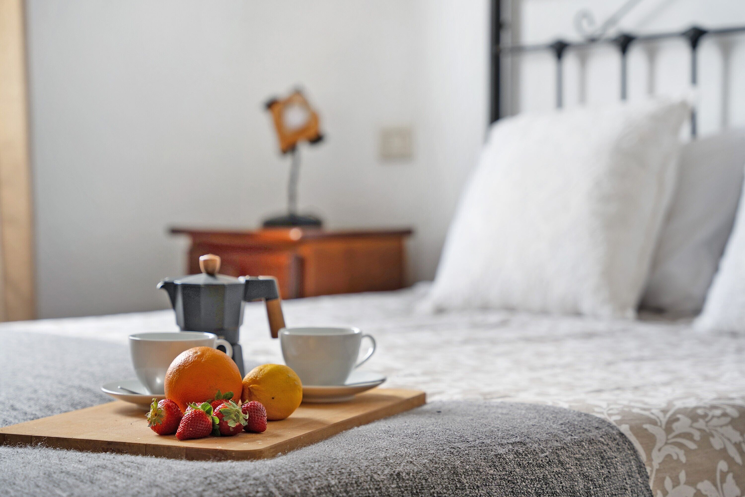 Een netjes opgemaakt bed met een dienblad met ontbijtartikelen, een koffiezetapparaat en een kleine tafellamp in een slaapkamer.