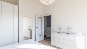 A bedroom with a bed, white wardrobe, dresser, and a door leading to another room.