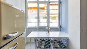 A kitchen with a white table and chairs, a vintage refrigerator, and a window with a view of a balcony.