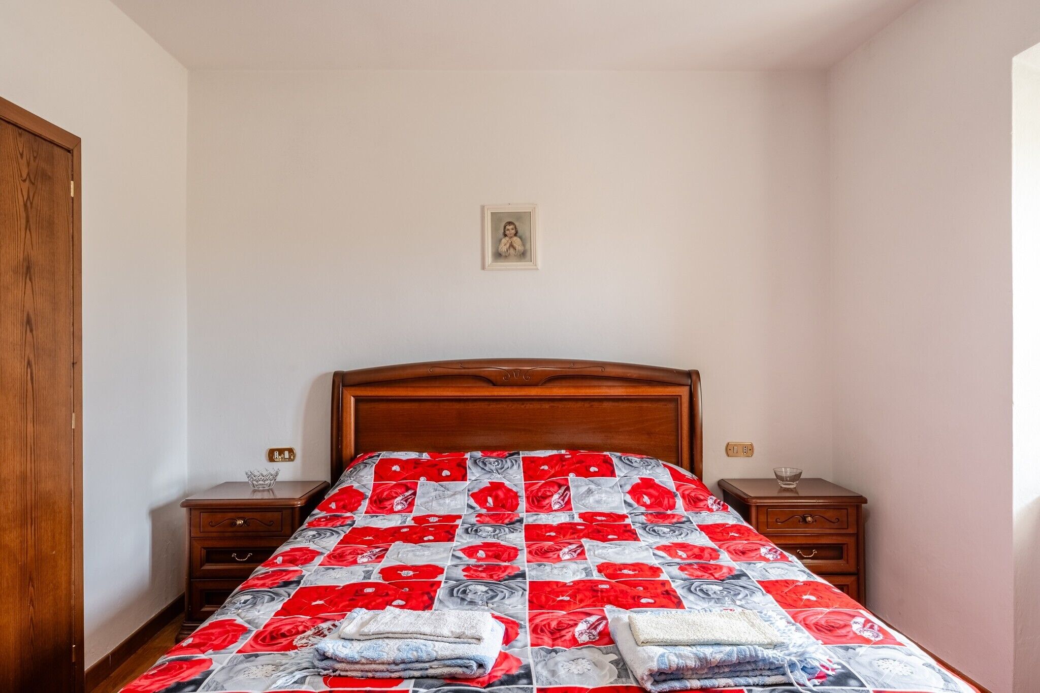 Ein Schlafzimmer mit einem hölzernen Bett, einem Nachttisch mit einem Glas und einem weiteren kleinen Nachttisch mit einer Schale.