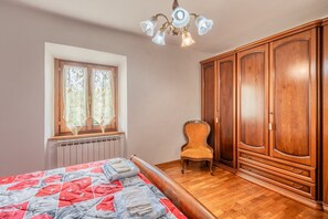 Makuuhuoneessa on sänky, ikkuna, jossa on verhot, tuoli ja puinen vaatekaappi.