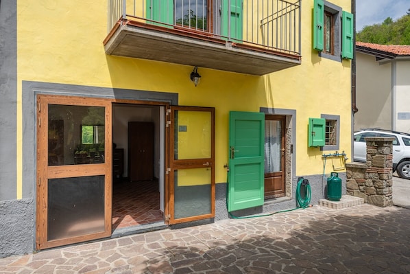 Un bâtiment jaune avec un balcon, une porte verte et une bouteille de gaz à l’extérieur.
