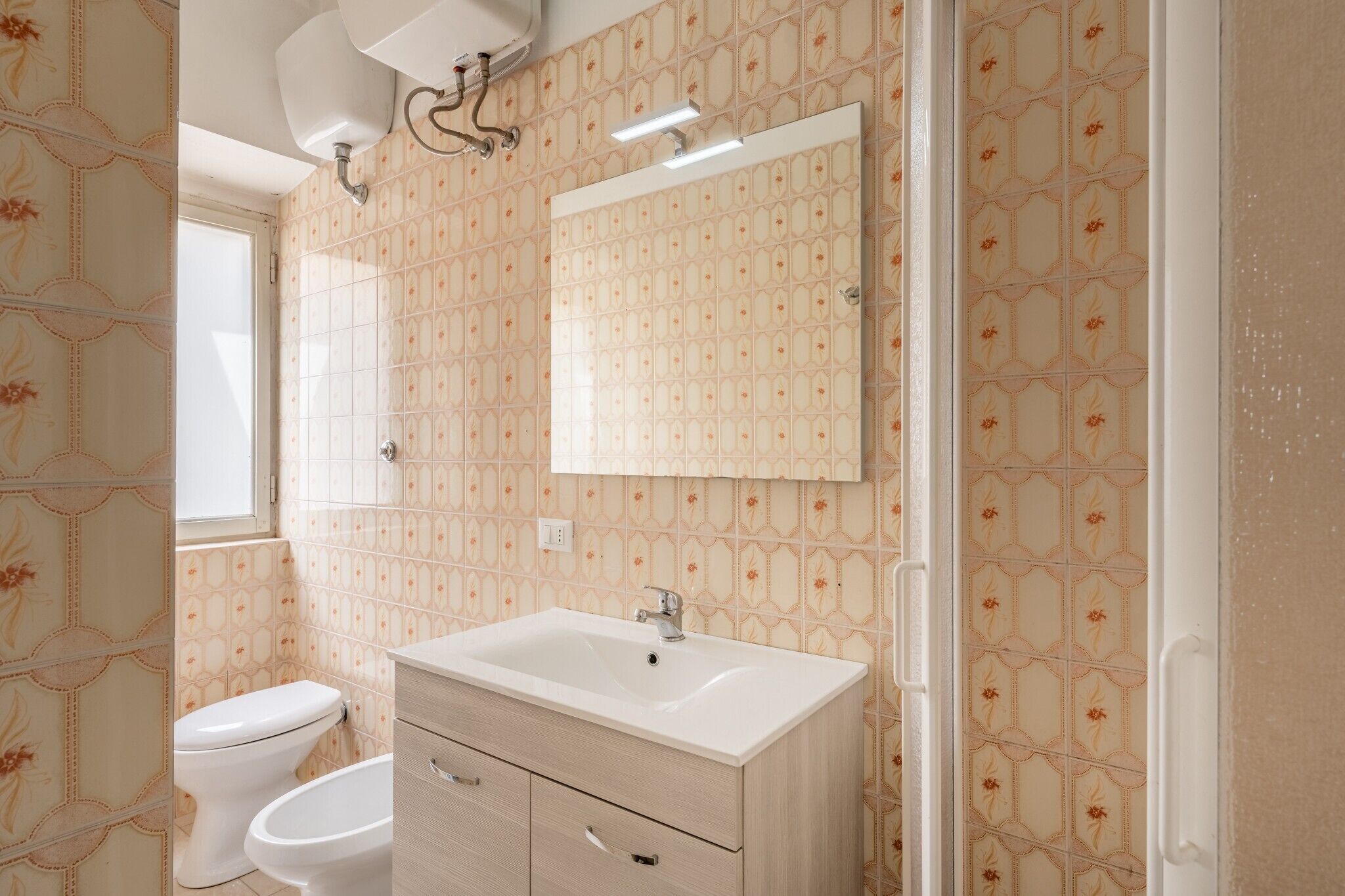Ein Badezimmer mit Toilette, Bidet, Waschtisch mit Spiegel und gemustertem Wandpapier.