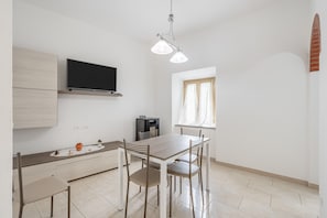 A modern kitchen with a dining table, chairs, a flat-screen TV, and a coffee machine.