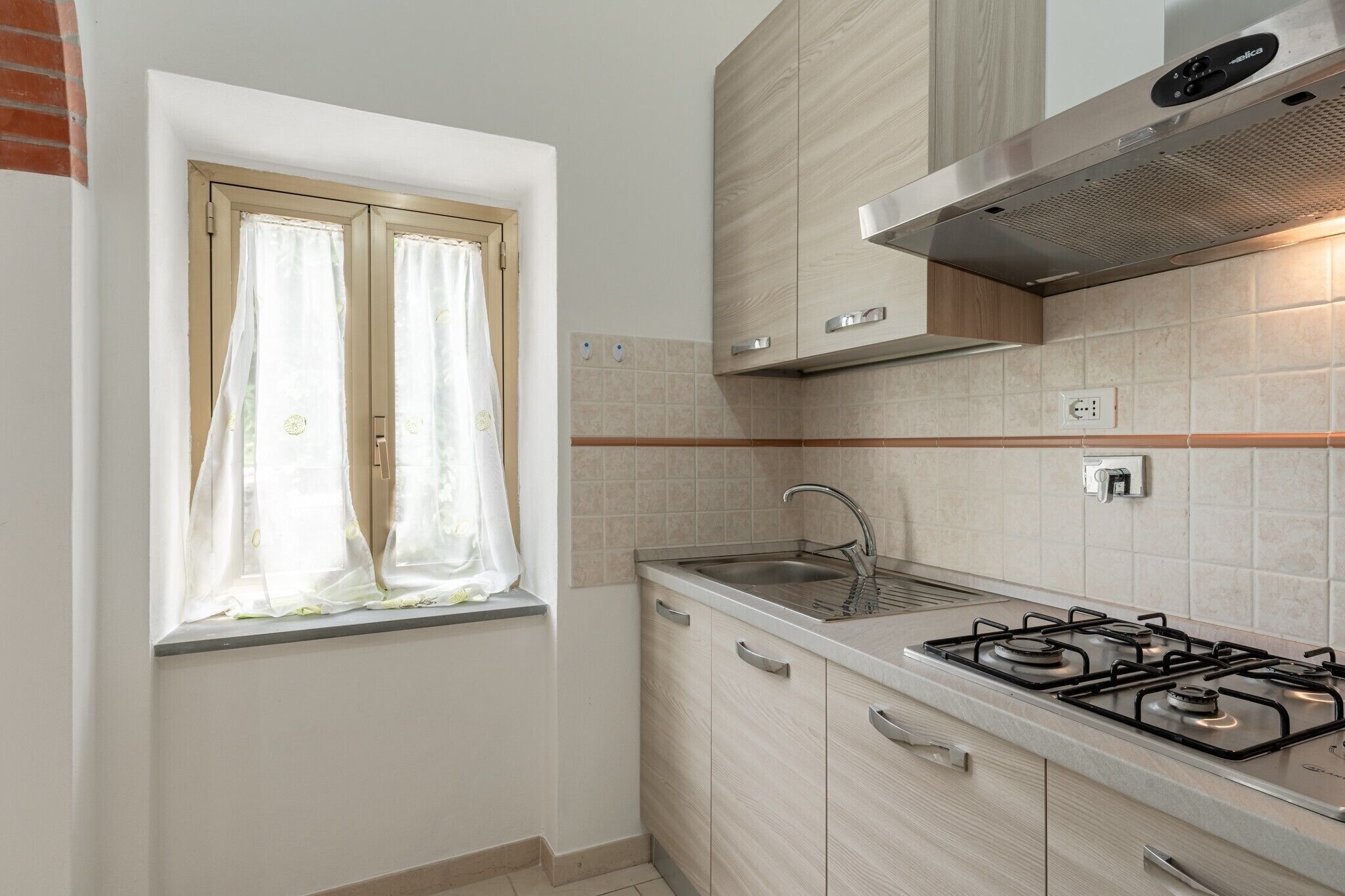 A kitchen with a window, a sink, a stove, and cabinets.