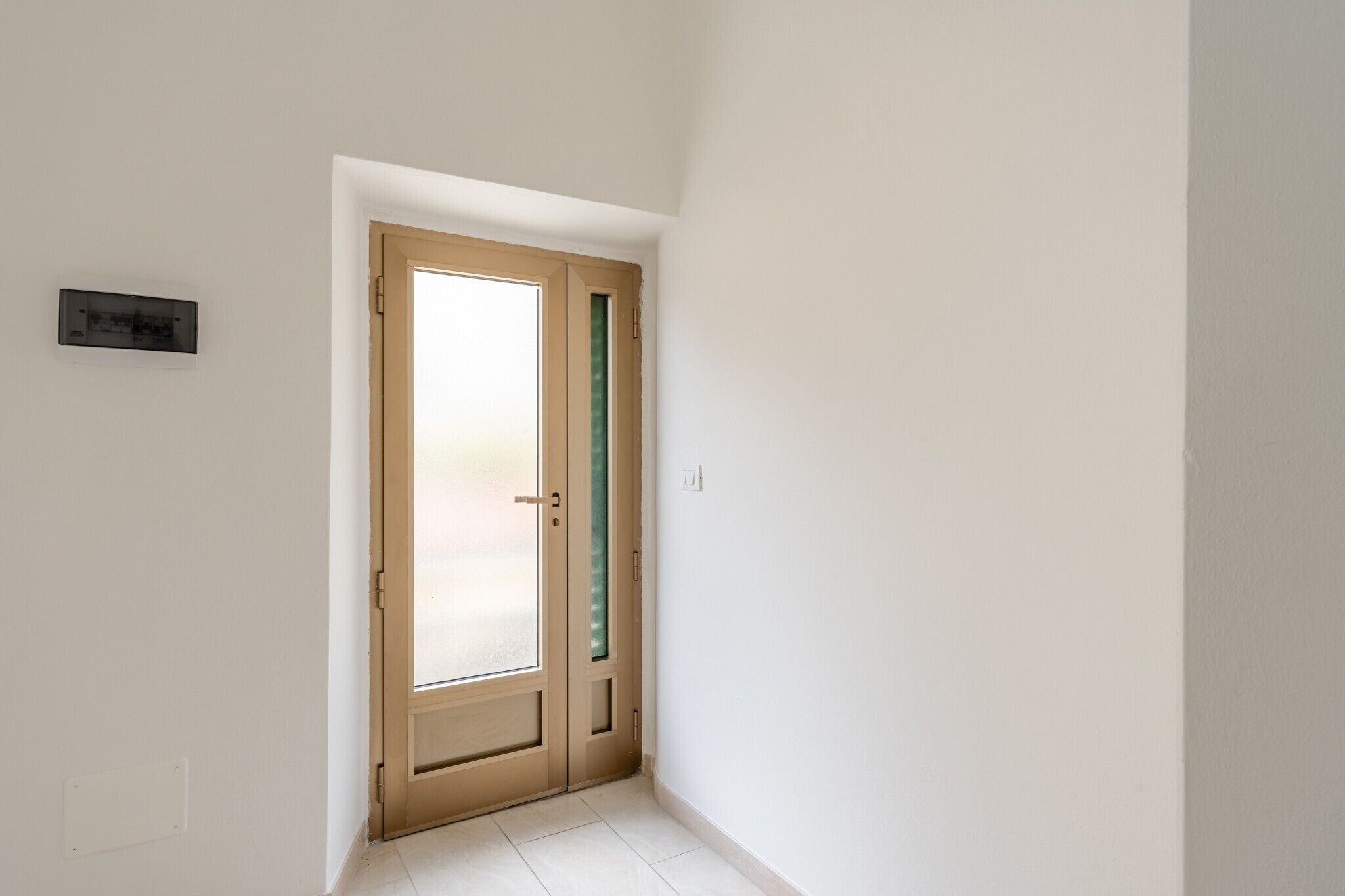 Un corridoio stretto con una porta in legno, un interruttore della luce e un piccolo dispositivo a parete.
