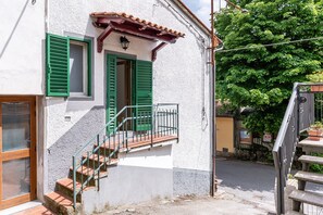 A white building with green shutters, a wooden staircase, and a metal railing.