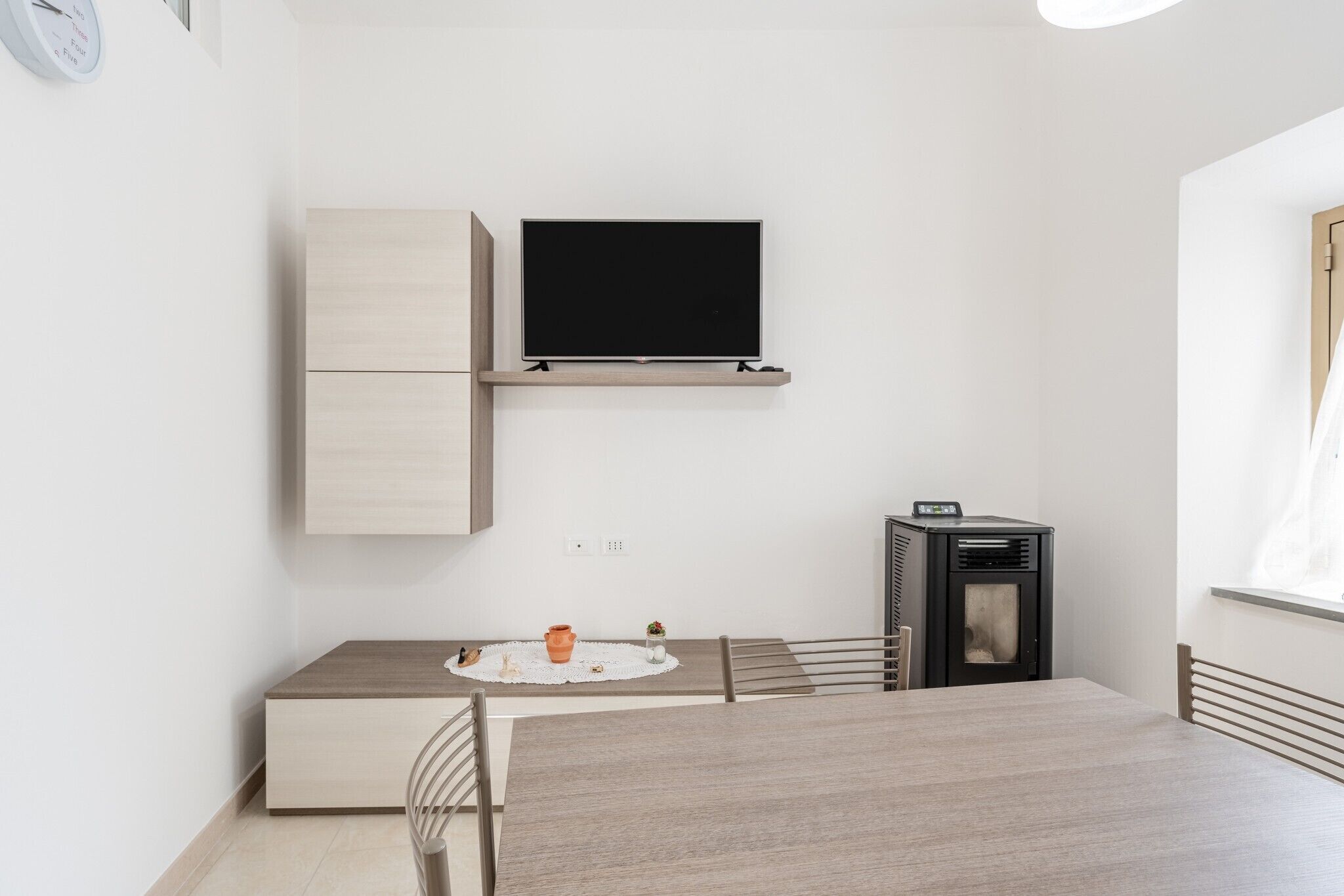 Une pièce au décor minimaliste, dotée d’un téléviseur à écran plat, d’un petit radiateur et d’une table à manger avec des chaises.