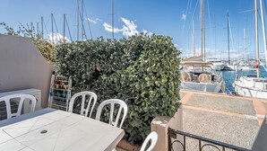 A patio with a table and chairs, a hedge, and a marina with boats in the background. - Apartment 'Résidence La Croisette' with Sea View and Private Terrace (Agde)