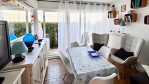 A modern living room with a dining area, a television, and a view of the outdoors. - Apartment 'Résidence La Croisette' with Sea View and Private Terrace (Agde)