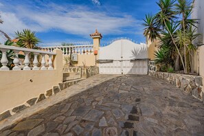 Un camino pavimentado que conduce a una entrada con portón, una pared de piedra y una estructura pequeña que parece una torre.