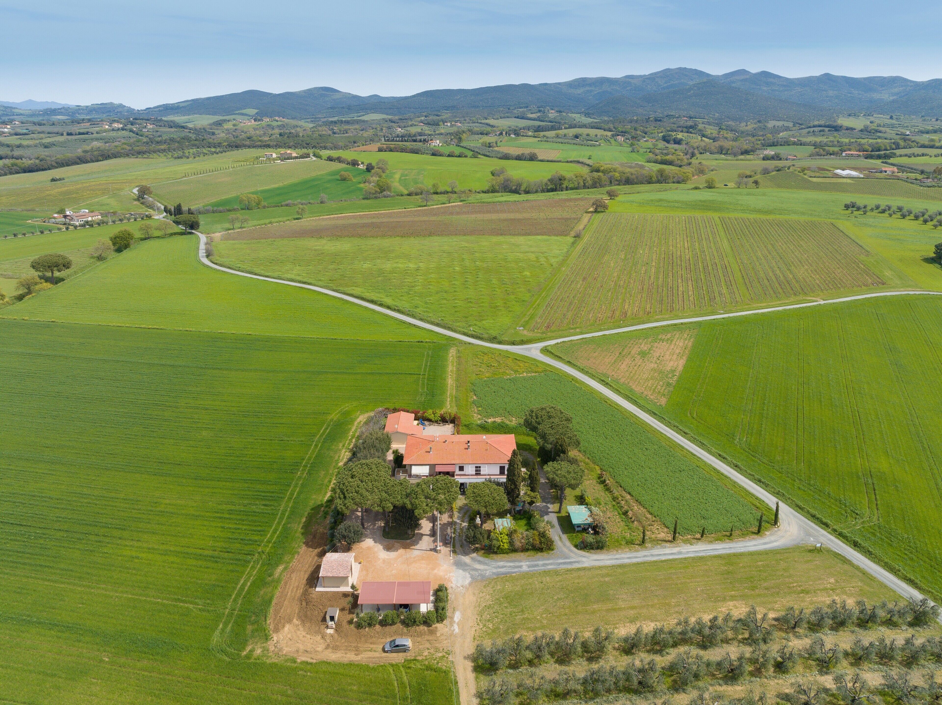 Vista aerea di un paesaggio rurale con campi, una strada e una casa con tetto rosso.