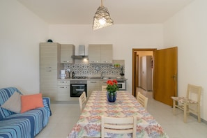 A compact living space with a dining table, chairs, a sofa, a kitchen area, and a door leading to another room.