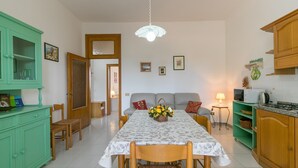 Un comedor con una mesa dispuesta para cuatro, un armario verde, un sofá y una zona de cocina con un microondas.