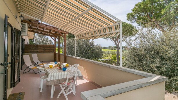 Ein Balkon mit gestreifter Markise, einem Tisch mit Stühlen und Blick auf Bäume und Grünflächen.