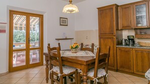 Ein Essbereich mit Holztisch und -stühlen, einer Hängeleuchte, einer Küche mit Holzausstattung und Blick durch eine Glastür.