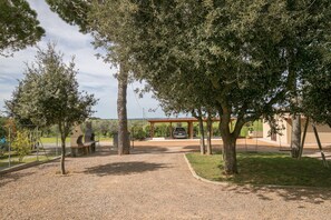 Un vialetto sterrato conduce a un'area coperta, con un'auto parcheggiata nelle vicinanze, il tutto circondato da alberi e da una recinzione.