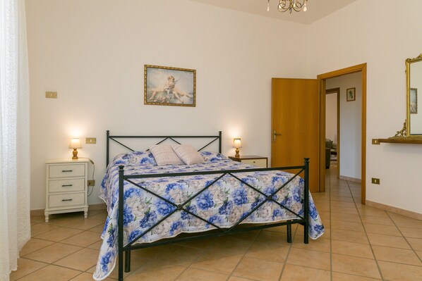 A bedroom with a bed, bedside tables, a nightstand, a mirror, and a door leading to another room.