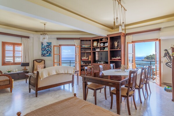 A spacious living room with a large dining table, a sofa, and a view of the sea.