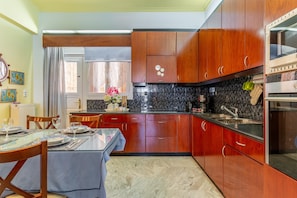 A kitchen with wooden cabinets, a marble countertop, and a dining area with a glass table and chairs.
