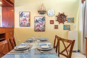 Un comedor con una mesa lista para cuatro, sillas de madera y adornos en la pared, incluyendo una rueda de barco y obras de arte enmarcadas.