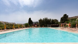 A swimming pool with lounge chairs and umbrellas, surrounded by greenery and buildings. - Villa Margi with Sea View, Shared Pool, Private Terraces and Wi-Fi (Scopello)