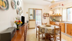 A kitchen with wooden cabinets, a dining table with chairs, a ceiling fan, and a microwave. - Villa Margi with Sea View, Shared Pool, Private Terraces and Wi-Fi (Scopello)