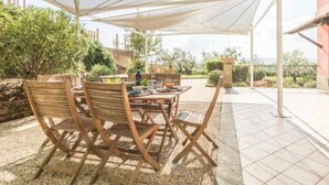 Un patio exterior con muebles de madera, una mesa lista para comer y un toldo blanco que da sombra.