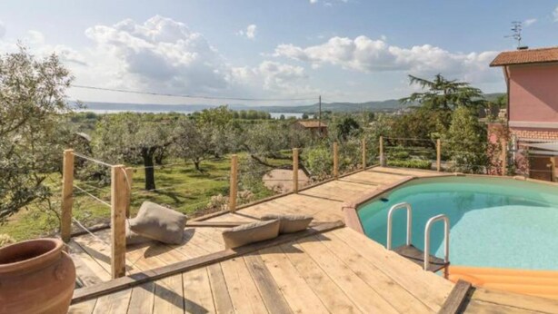 Una terraza de madera con piscina, rodeada de vegetación y un cielo despejado.