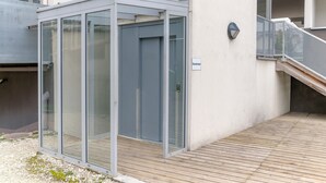 A modern building with a glass enclosure, a wooden deck, and a metal staircase.