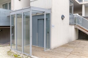 A modern building with a glass enclosure, a wooden deck, and a metal staircase.