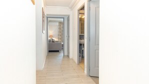 A hallway with a light-colored wooden floor, a grey sofa in the background, and a door leading to a bathroom.