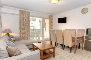 A living room with a sofa, a coffee table, a dining table with chairs, a TV, and an air conditioning unit.