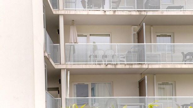 A multi-story building with balconies, each with a mesh railing and a door.