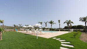 A pool area with lounge chairs and umbrellas, surrounded by palm trees and a grassy lawn. - Holiday Home 'Villa Gioberta, Fiori' with Shared Pool, Wi-Fi and Air Conditioning (Menfi)