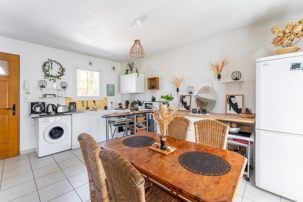 Et moderne køkken med et spisebord, stole, en vaskemaskine og diverse hårde hvidevarer.