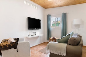 A living room with a flat-screen TV, a sofa, a chair, a small table, a lamp, and a window with curtains. - Holiday Apartment 'Casa Verol B' with Wi-Fi (Moya)