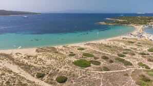 Vista aérea de una zona costera con playa, aguas cristalinas y un barco a lo lejos.