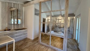 Una habitación con suelo de madera, un espejo grande, un banco de madera y una puerta corredera que da a un armario.