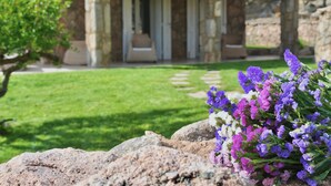 Un edificio de piedra con un porche cubierto, un camino de piedra y un jardín con flores moradas.