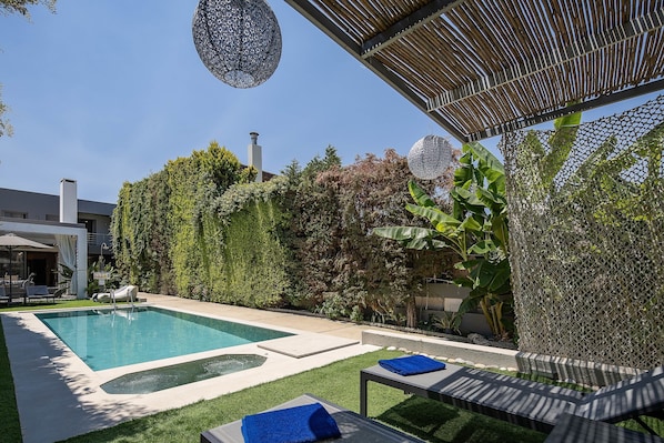 Una piscina con sillones de descanso, una pérgola y un seto.