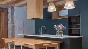 Una cocina moderna con vigas de madera, una isla central, una mesa de comedor con sillas, luces colgantes y un horno empotrado.