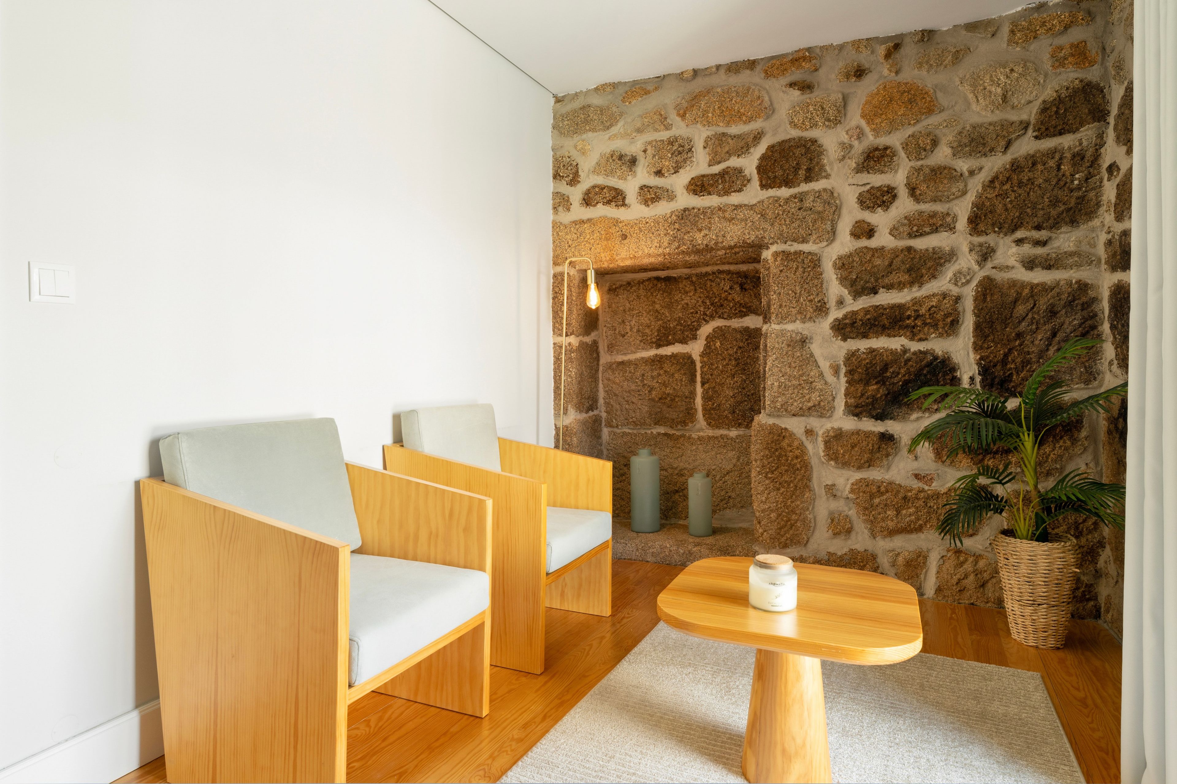 Una habitación moderna con una pared de piedra, dos sillas de madera, una mesita pequeña y una planta en maceta.