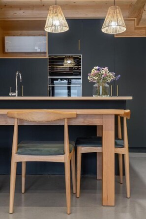 A modern kitchen with a central island, wooden chairs, and pendant lighting.